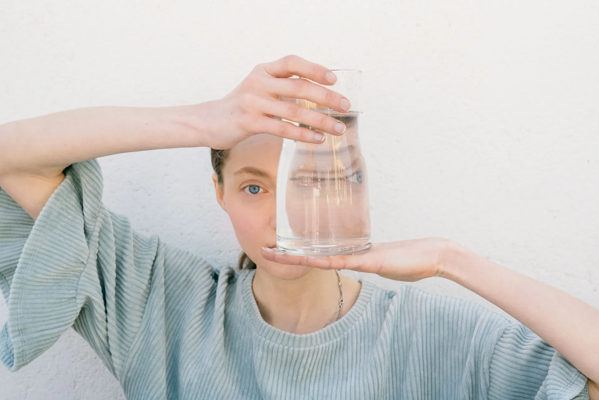 (c) pexels_leeloothefirst_Person hält ein Glas Wasser vor dem Auge. Sie trägt ein hellblaues T-Shirt mit Rüschen an den Ärmeln.