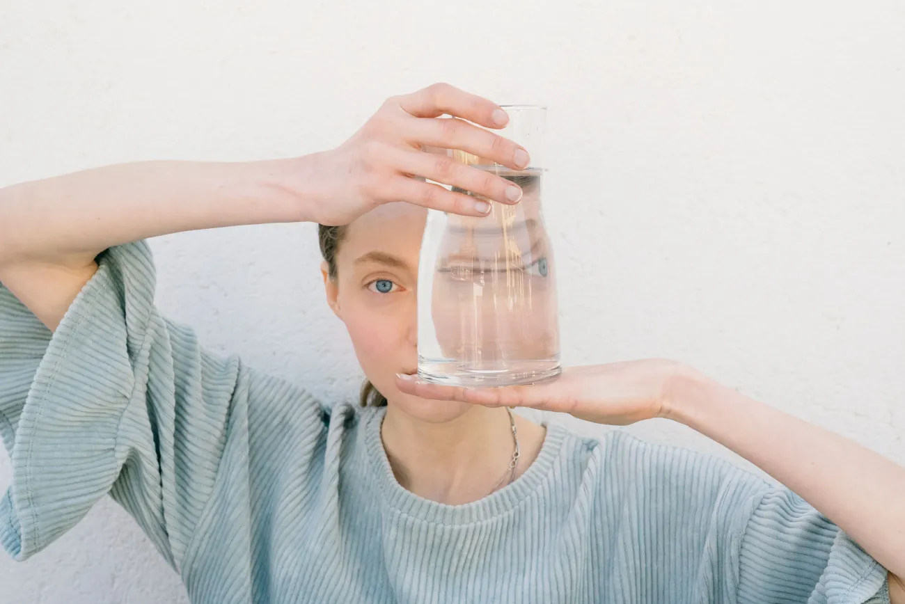 (c) pexels_leeloothefirst_Person hält ein Glas Wasser vor dem Auge. Sie trägt ein hellblaues T-Shirt mit Rüschen an den Ärmeln.