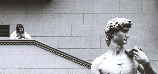 Statue „David“ von Michelangelo, im Hintergrund fotografiert eine Person die Skulptur mit einem Smartphone.