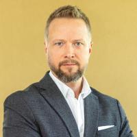 Porträt von Assoc. Prof. Mag. Dr. Michael Wininger. Er hat einen Bart und kurze, blonde Haare. Er trägt ein dunkles Sakko und ein weißes Hemd. Er blickt neutral in die Kamera. Der Hintergrund ist einfarbig in warmem Gelb.