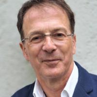 Porträt einer Person mit Brille und freundlichem Lächeln.