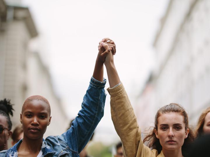 Zwei Frauen gehen auf einer Straße und halten ihre Hände gemeinsam nach oben (c) shutterstock_Jacob Lund