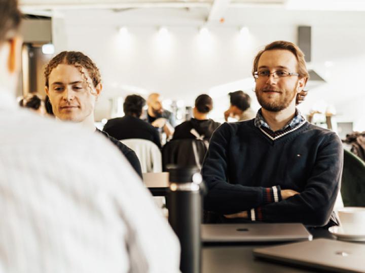 Personen sitzen in einem Lehrraum und hören einer vortragenden Person zu, die angeschnitten von hinten im Bild zu sehen ist (c) pexels-bertellifotografia